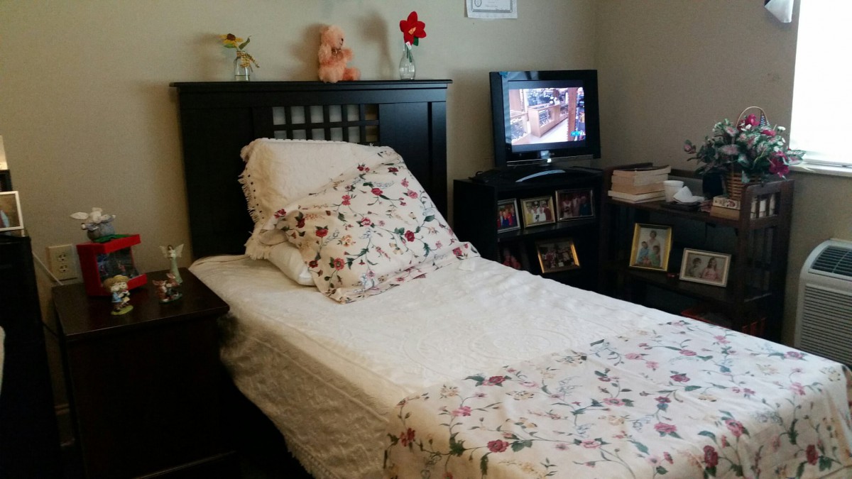 A cozy bedroom with a bed featuring floral bedding and a TV on a shelf.