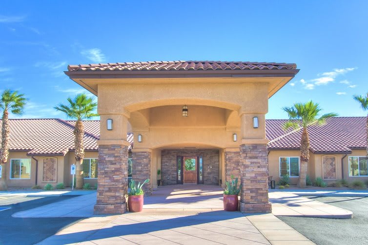 A sunny view of a building entrance with a covered walkway and palm trees.