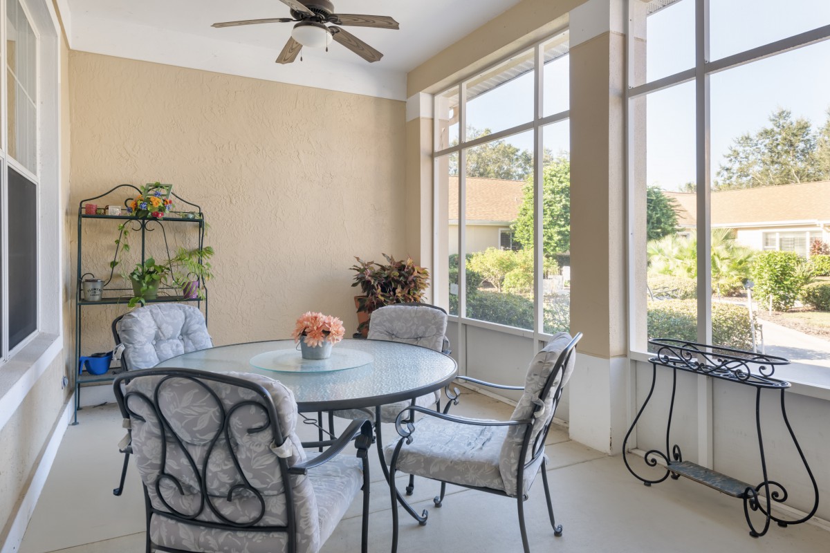 A bright and airy patio with a round table and chairs, surrounded by large windows and decorated with plants.