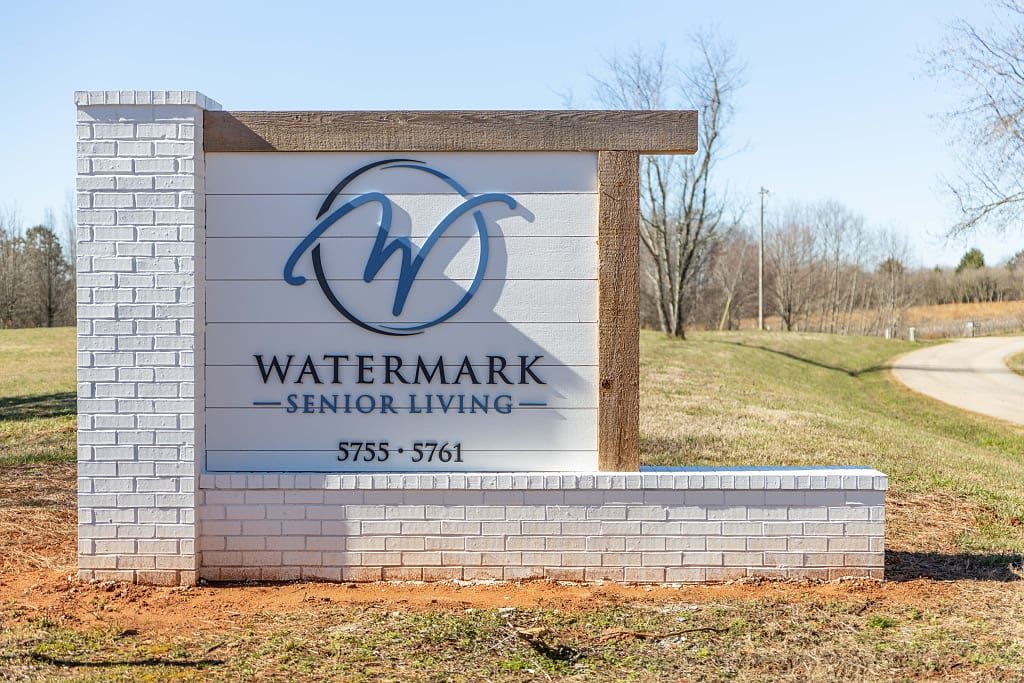 A sign for Watermark Senior Living located outdoors, featuring a brick base and wooden accents.