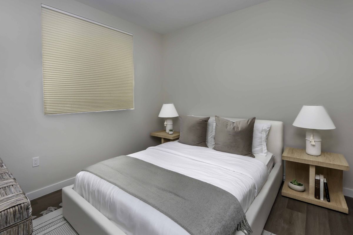A modern, minimalist bedroom featuring a neatly made bed with gray accents and two side tables with lamps.