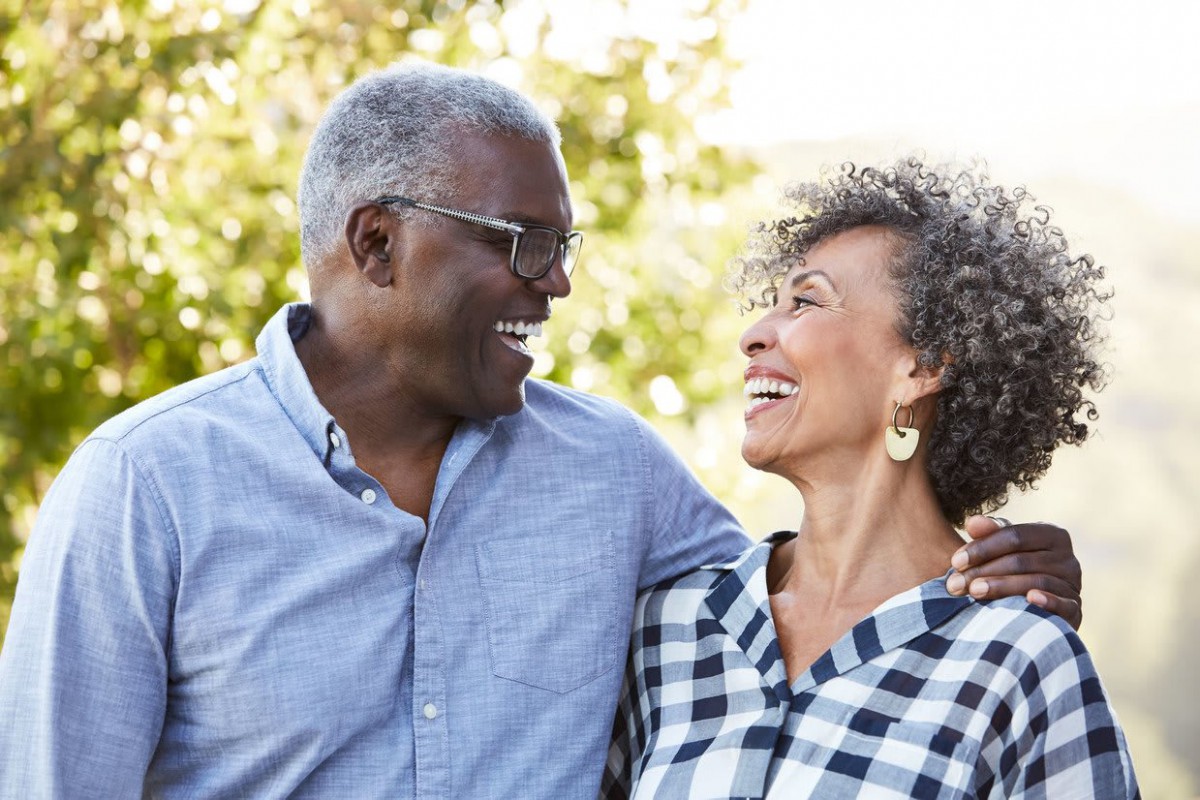 An elderly couple smiling at each other outdoors.