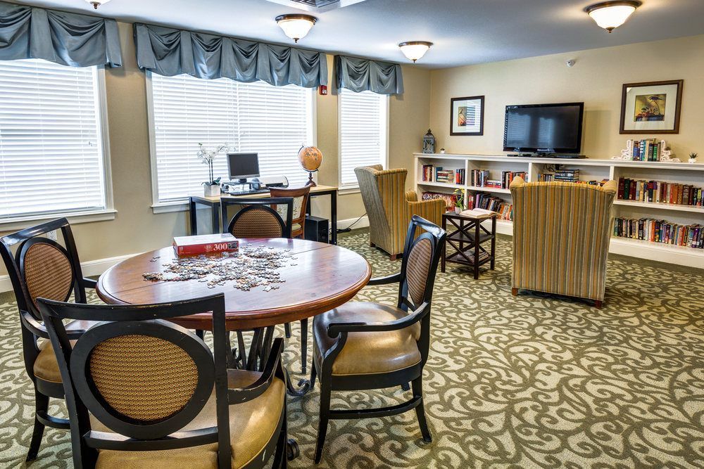 A cozy living room with a round table, chairs, a computer desk, bookshelf, and television.