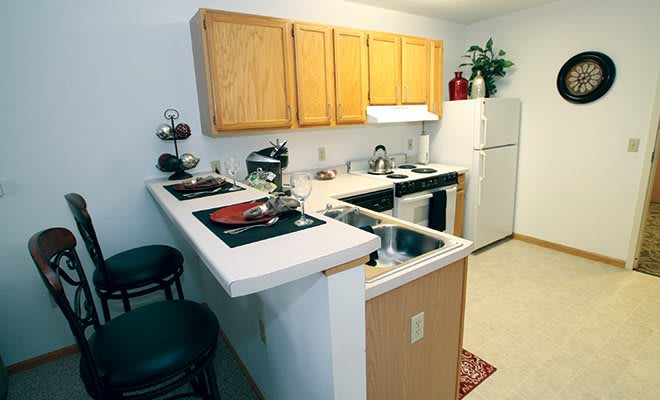 A compact kitchen with wooden cabinets, a white countertop, and bar seating.
