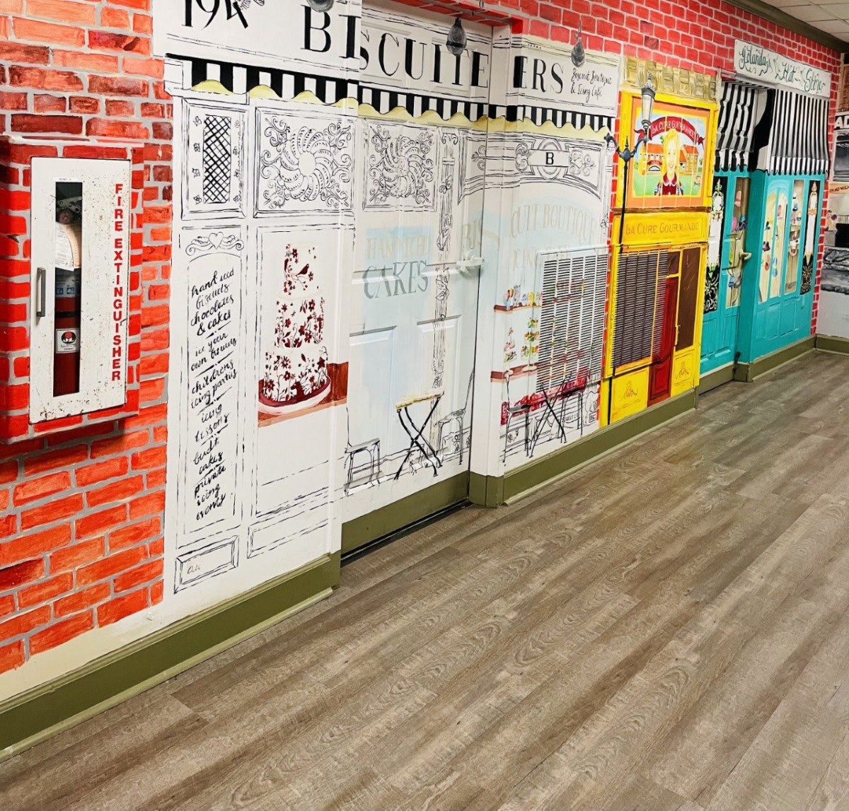 Colorful indoor wall murals depicting shop facades along a hallway.