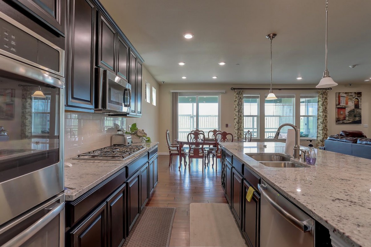 A modern kitchen with dark cabinets, a large island, and a dining area in an open-concept layout.