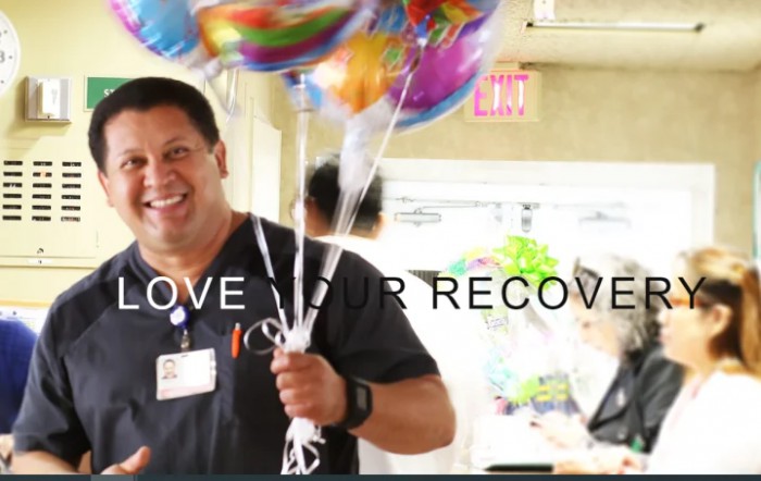 A healthcare worker smiling and holding a bunch of colorful balloons in a hospital setting.