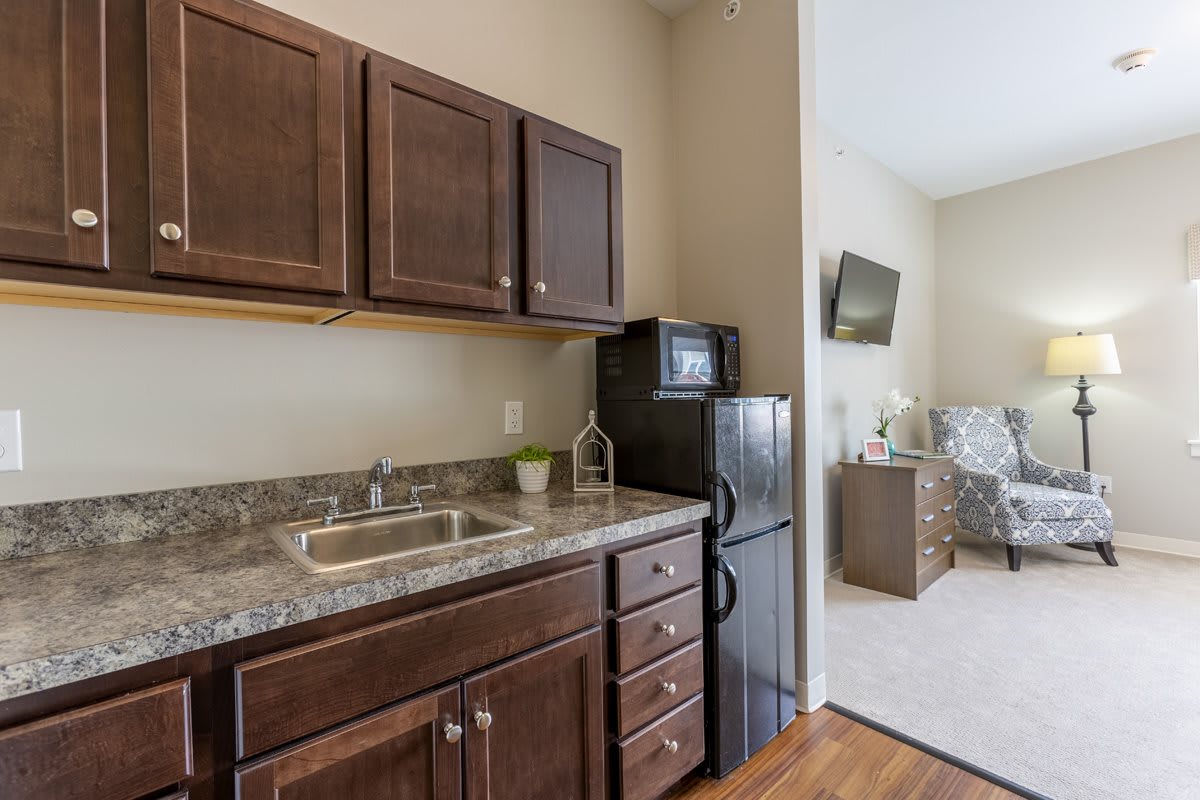 A compact kitchenette with wooden cabinets, countertop, sink, microwave, and refrigerator.