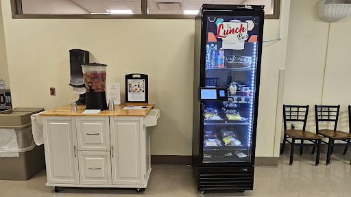 A modern vending machine offering various snacks and beverages, located in an office or break room setting.