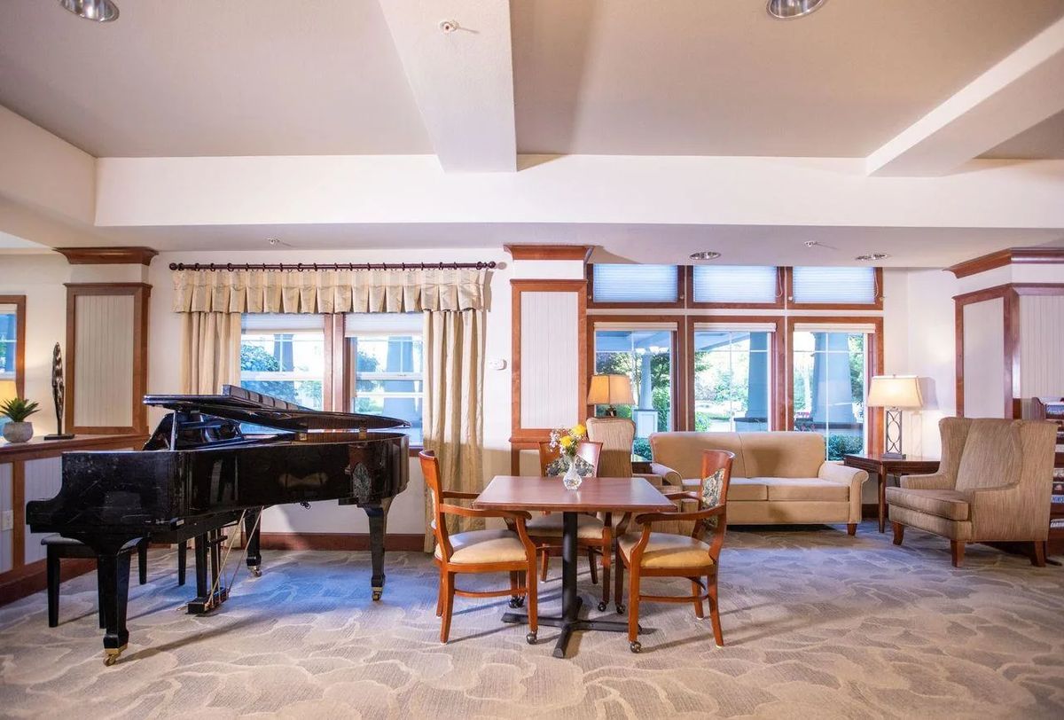 A cozy living room with a grand piano, table, chairs, and a sofa near large windows.
