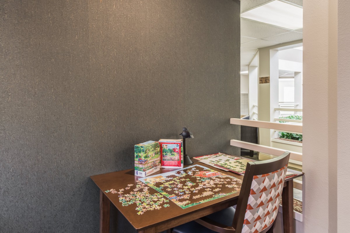 A cozy indoor setup featuring a table with a partially completed jigsaw puzzle, accompanied by a lamp and chair.