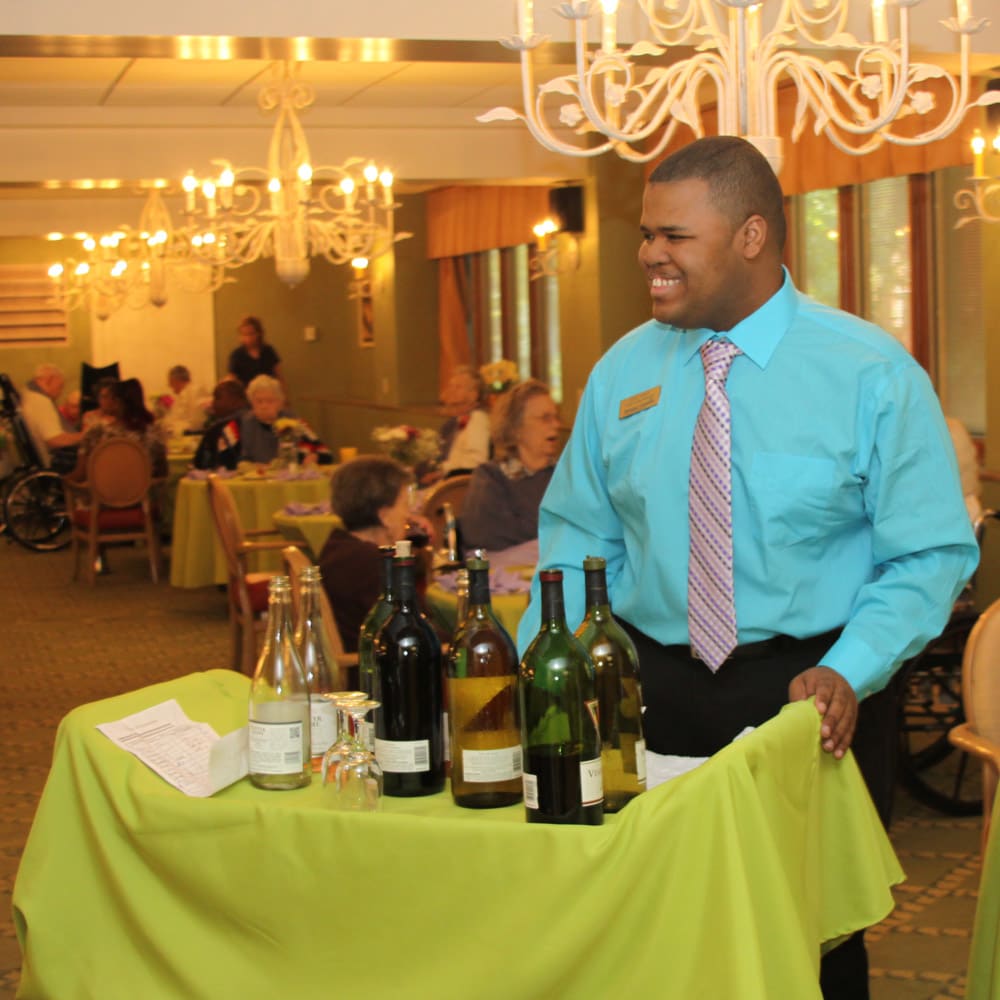 A waiter in formal attire serves wine bottles at a restaurant event.