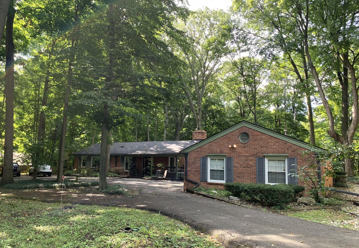 A brick house surrounded by trees with a driveway in the foreground.