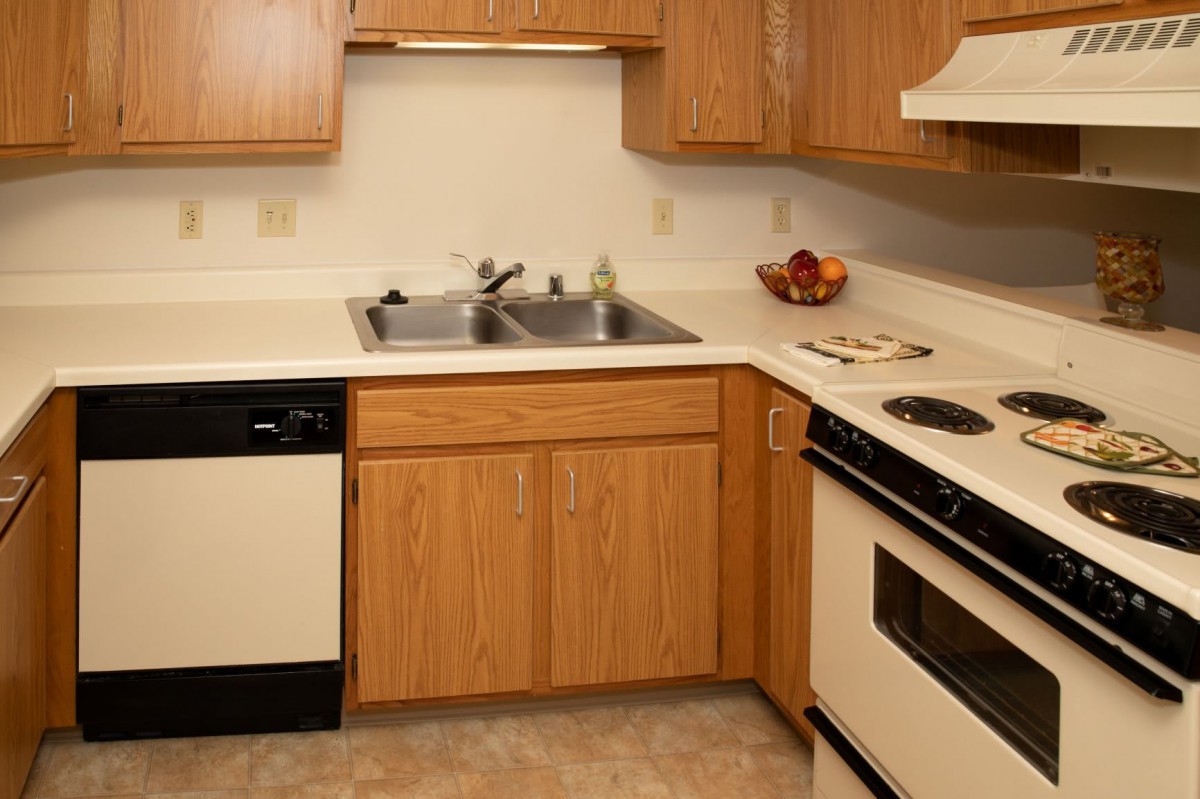 A compact kitchen featuring wooden cabinets, a stainless steel sink, and standard appliances.