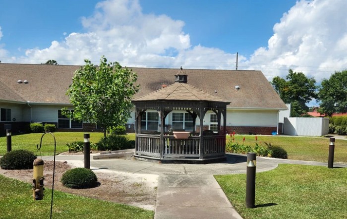 A wooden gazebo situated in a landscaped garden with a building in the background.