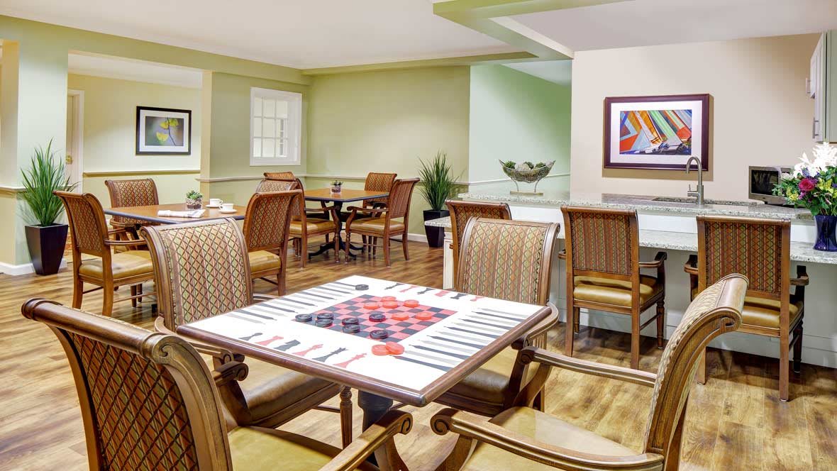 A cozy dining area featuring a game table, surrounded by wooden chairs and decorated with artwork and plants.