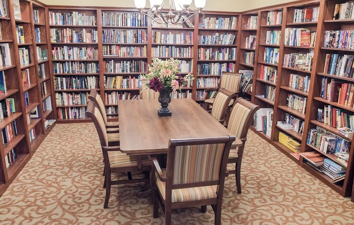 A quiet library reading room with a wooden table and chairs surrounded by bookshelves.