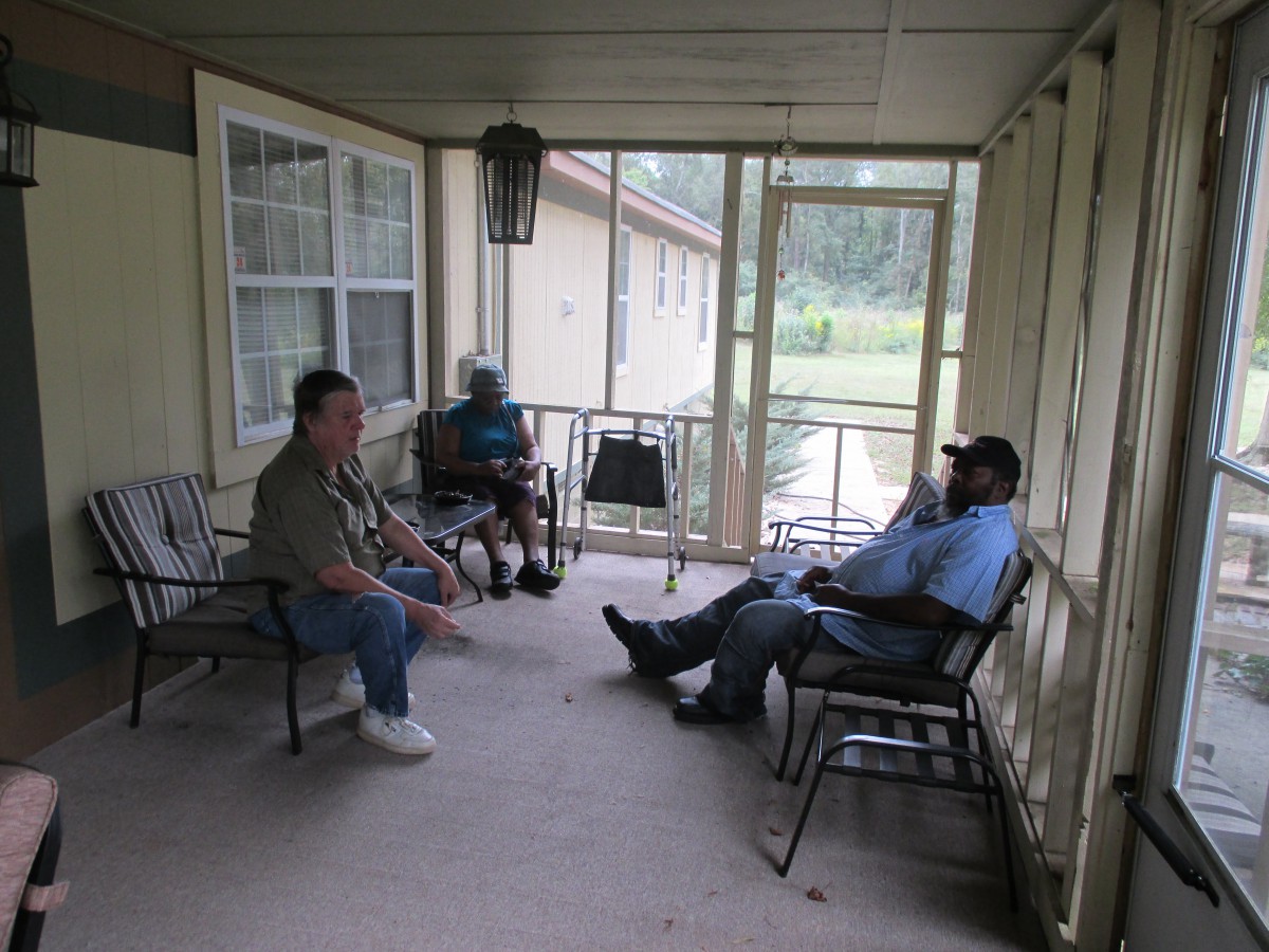Three people sitting and conversing on a porch.