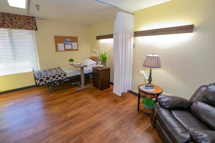 A cozy hospital room with a bed, seating area, and decorative elements.