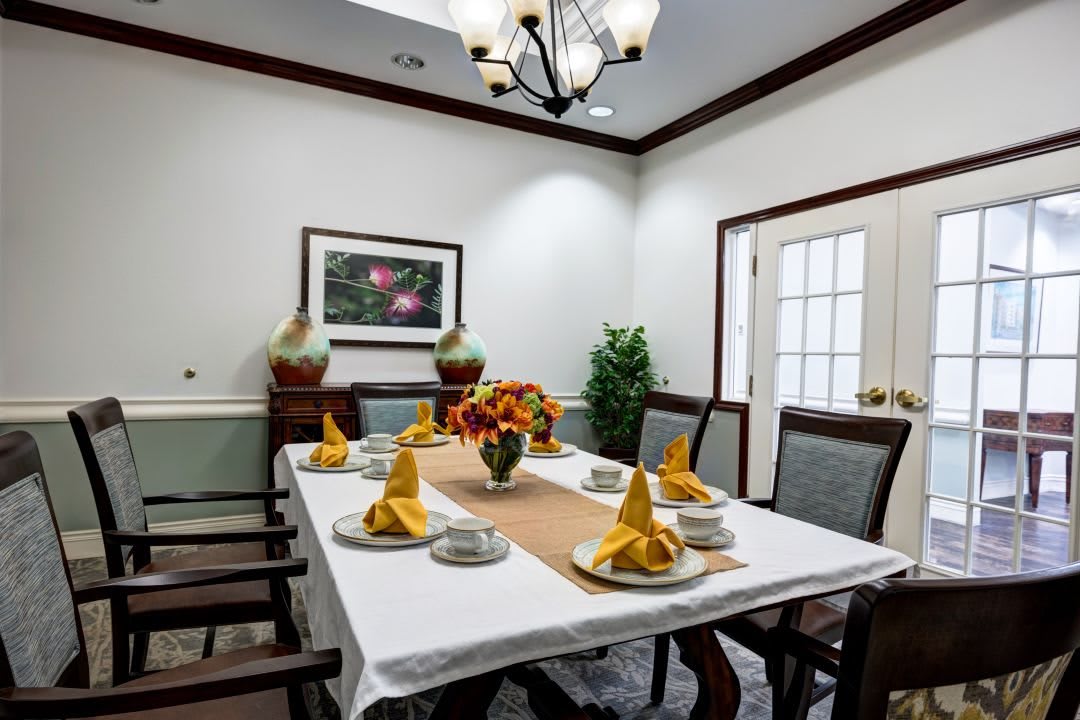 A neatly arranged dining room with a table set for six, featuring yellow napkins and a floral centerpiece.