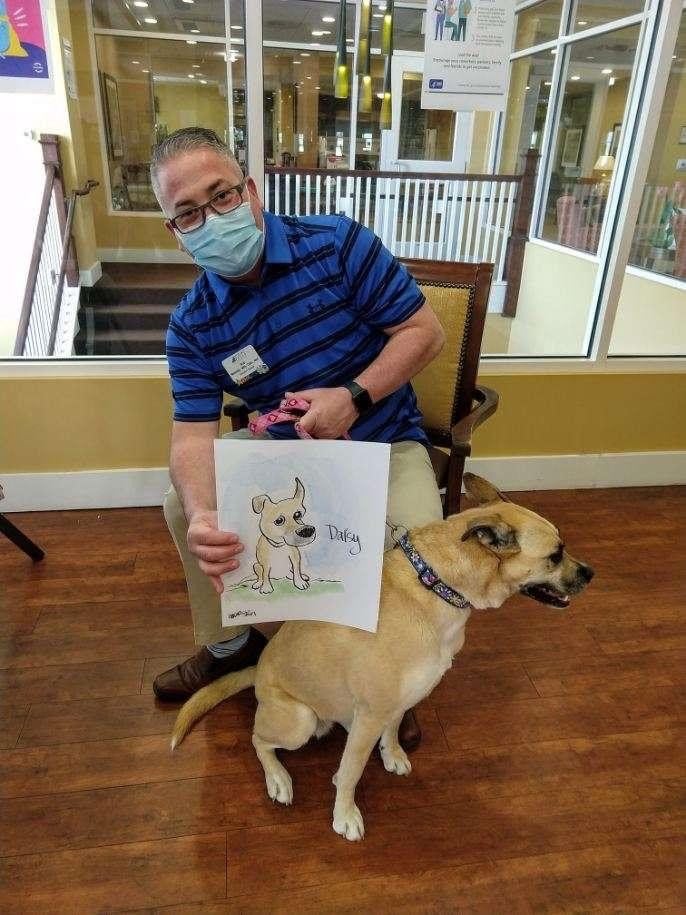 A person wearing a mask holds a drawing of a dog next to an actual dog.