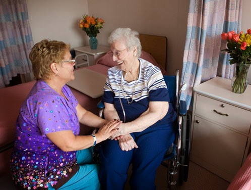 A caregiver lovingly interacts with an elderly woman in a hospital room, highlighting the importance of compassion and support in healthcare.