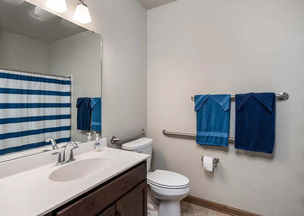 A neatly organized bathroom featuring a sink, toilet, and blue towels.