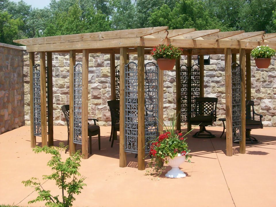 A wooden pergola adorned with hanging plants, set on a patio against a stone wall backdrop.