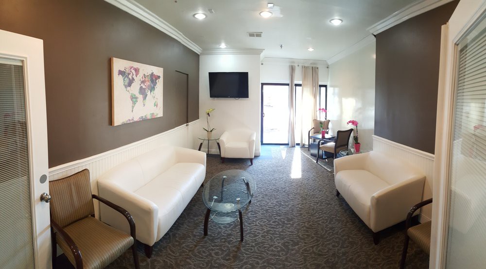 A modern waiting room featuring white sofas, a television, and decorative artwork on the walls.
