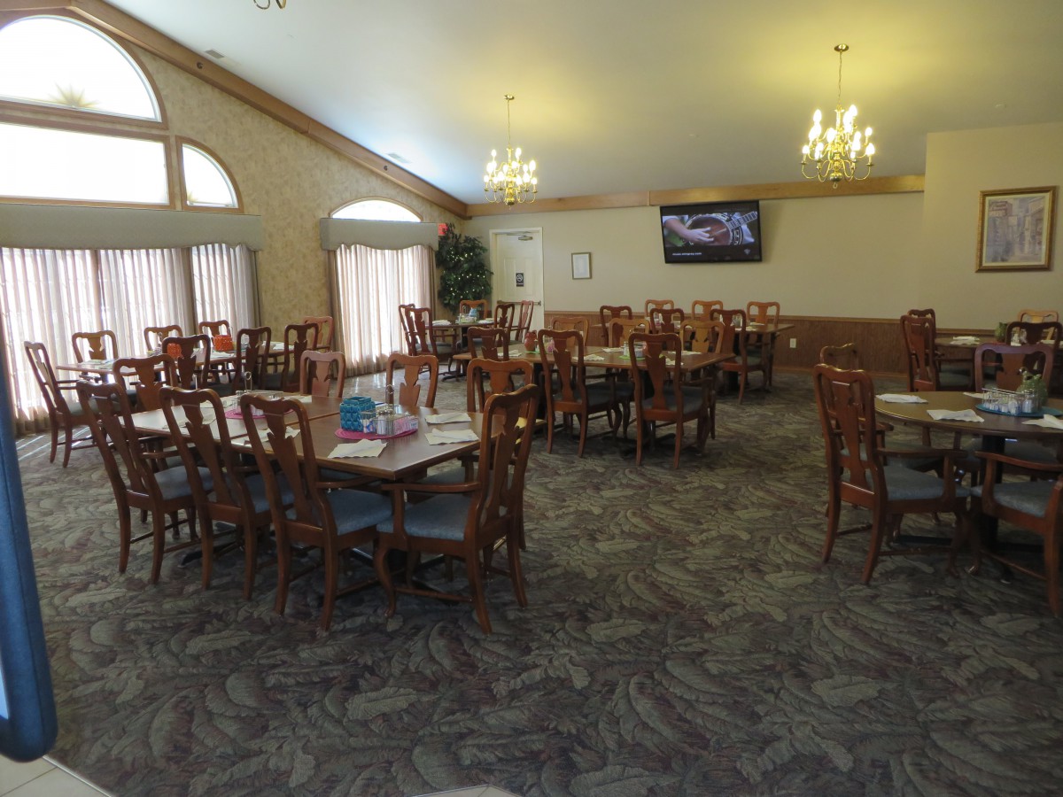 A spacious dining room with multiple tables and chairs, featuring a television and chandeliers.