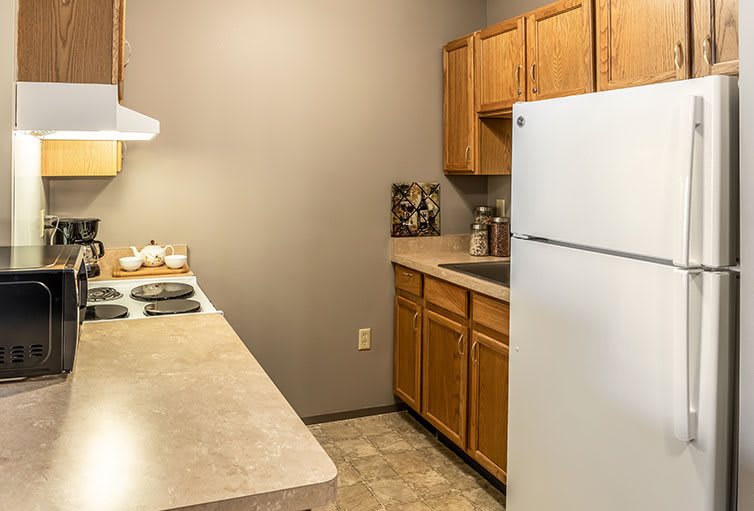 A small kitchen with wooden cabinets, a refrigerator, stove, and sink.