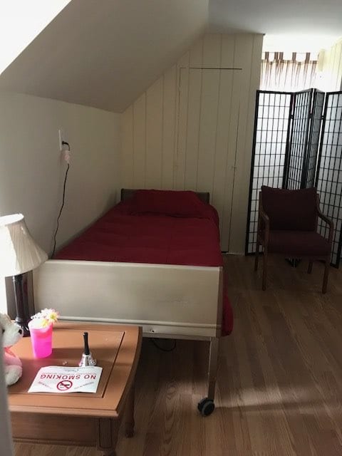 A simple bedroom with a single bed, a lamp on a table, and a screen divider.