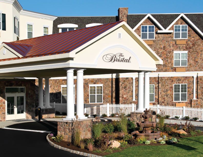 The entrance of a hotel with stone fa�ade and landscaped surroundings.