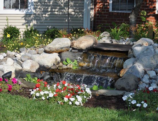 A small waterfall feature in a landscaped garden with colorful flowers and rocks.