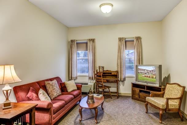A cozy living room with a red sofa, coffee table, TV, and curtains.