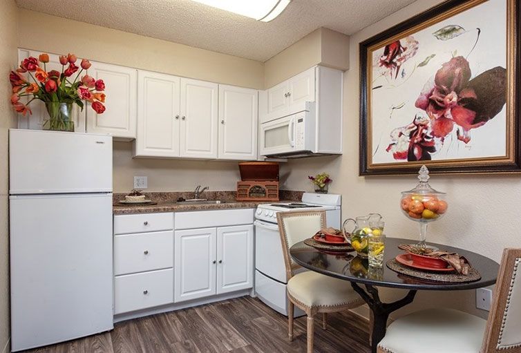 A cozy kitchen with white cabinets, a small dining table, and decorative artwork.