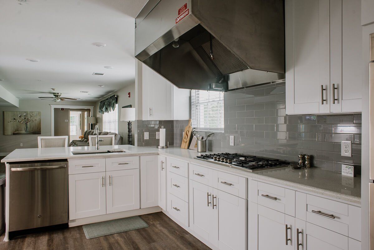 A modern kitchen with white cabinets, a stainless steel vent hood, and a gas stove.