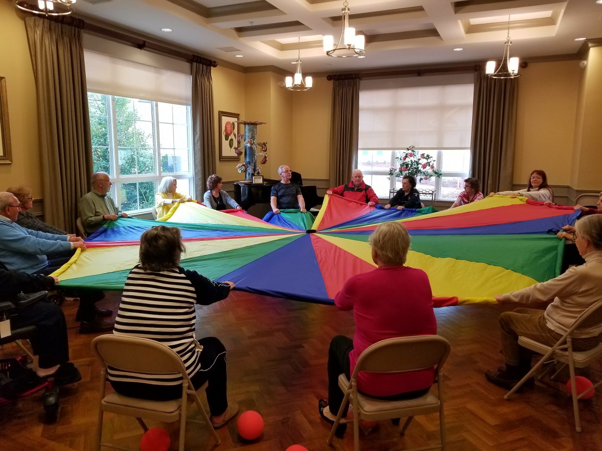 A group of elderly individuals engage in a fun indoor activity with a colorful parachute.