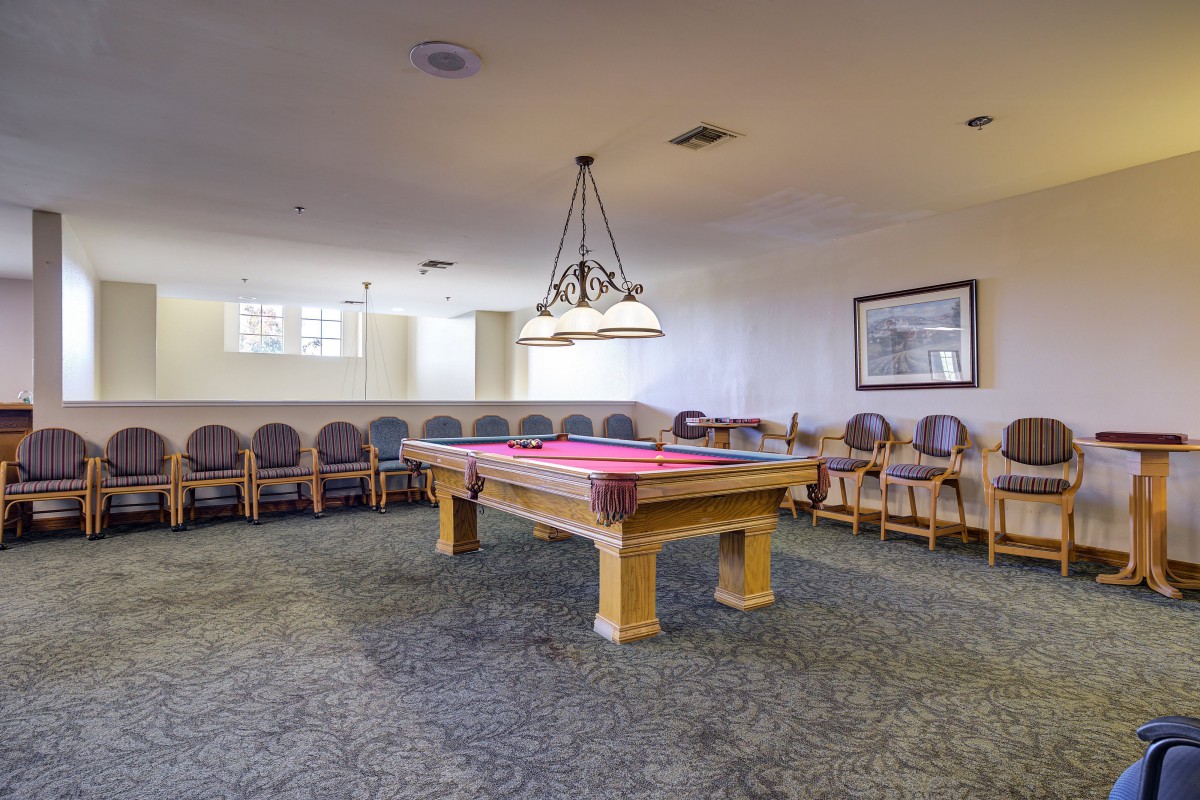 A spacious billiard room featuring a pool table with overhead lighting and a seating area along the wall.