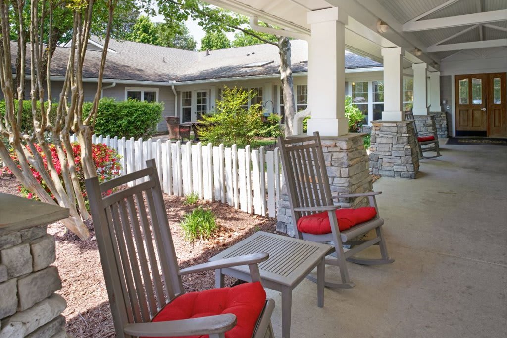 A cozy porch with wooden rocking chairs featuring red cushions, overlooking a garden area.