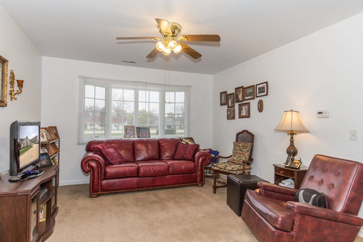 A cozy living room featuring red leather furniture, including a sofa and armchair, with a ceiling fan and decorative frames on the wall.