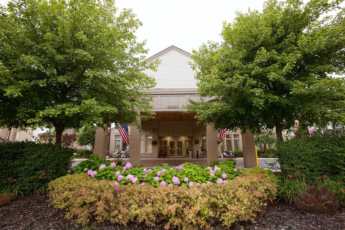 Front view of a building entrance with lush greenery and colorful flowers.
