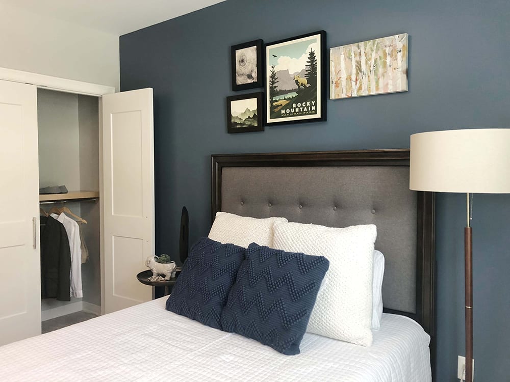 A cozy bedroom with a blue accent wall, decorated with framed artwork above a neatly made bed featuring navy pillows.