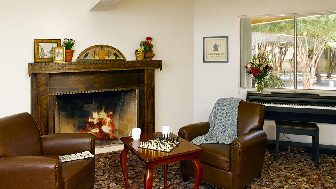 A cozy living room with a fireplace, two armchairs, and a chess game on the table.
