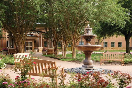 A serene garden featuring a central fountain surrounded by benches and vibrant flower beds.