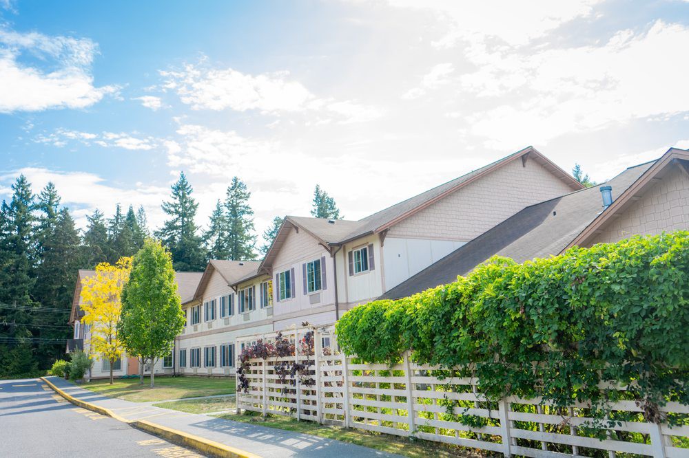 A suburban residential building with a white fence and surrounding trees on a sunny day.