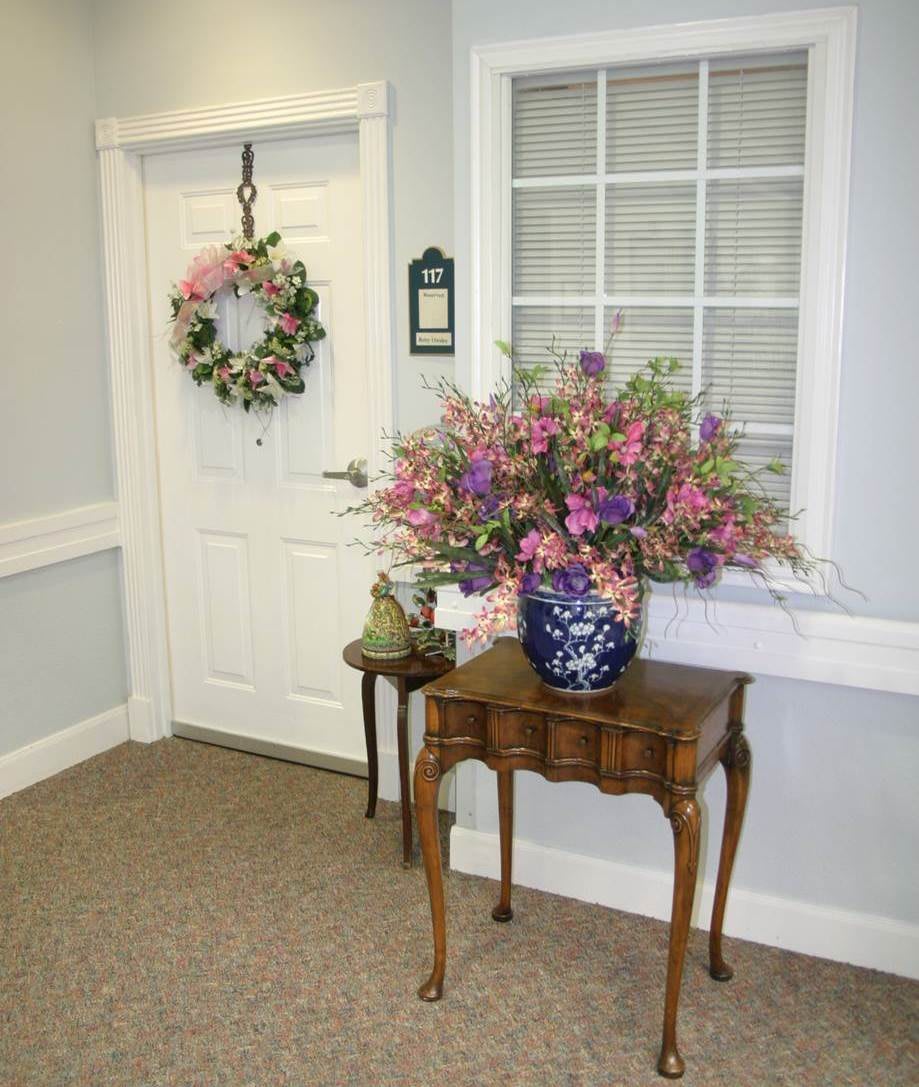 A small hallway with a wooden table adorned with a floral arrangement next to a door with a wreath.