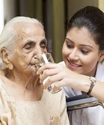 A caregiver assists an elderly woman with drinking water.