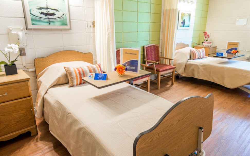 A well-lit hospital room with two beds, featuring comfortable furnishings and medical equipment.