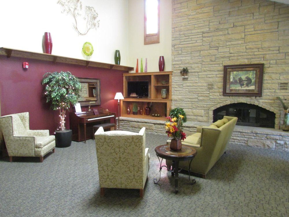 A cozy living room with a sofa, chairs, and a fireplace, featuring warm decor and indoor plants.